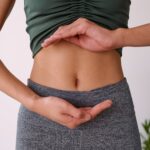 Close-up of a woman's abdomen. She is holding her hands in front of her stomach to frame her belly button.