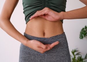 Close-up of a woman's abdomen. She is holding her hands in front of her stomach to frame her belly button.